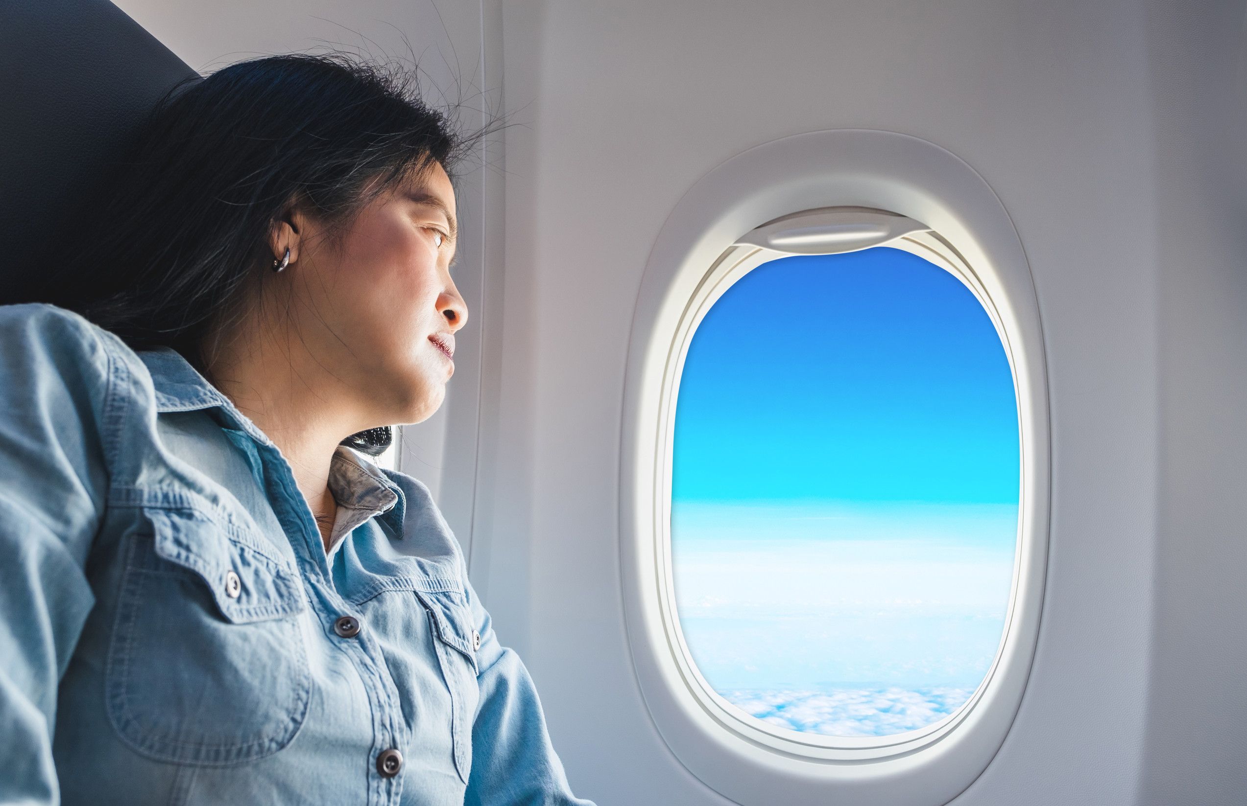 飛行機の窓側席に座るアジア人女性が窓の外を眺め、青空を眺める 飛行機の窓側席に座るアジア人女性が窓の外を眺め、青空を眺める