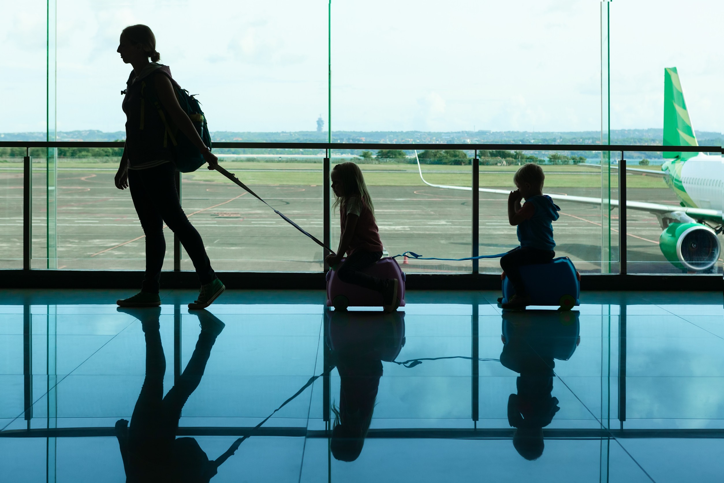 Nella sala di transito dell'aeroporto, una giovane madre porta con sé le valigie dei bambini piccoli fino al gate di partenza per Nella sala di transito dell'aeroporto, una giovane madre porta con sé le valigie dei bambini piccoli fino al gate di partenza per
