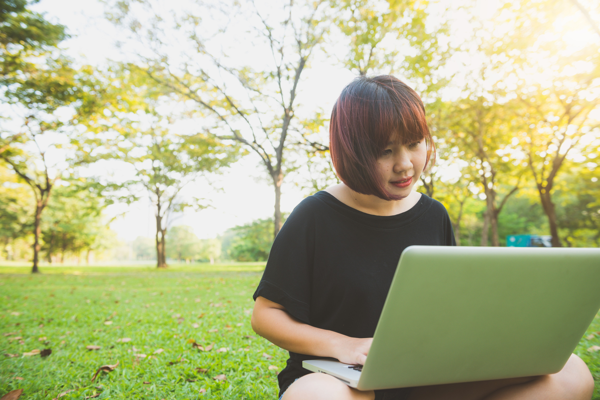 giovane donna asiatica con le gambe sull'erba verde e il computer portatile aperto, mani della ragazza sulla tastiera giovane donna asiatica con le gambe sull'erba verde e il computer portatile aperto, mani della ragazza sulla tastiera