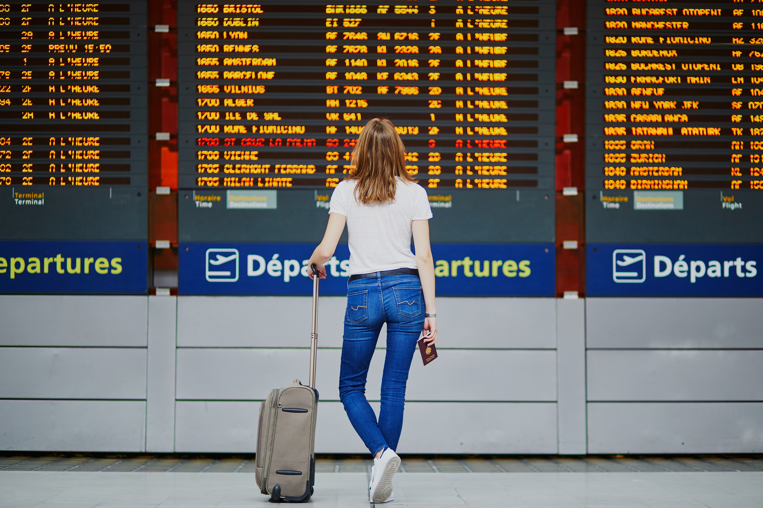 giovane donna in aeroporto internazionale con bagaglio e passaporto vicino al display informativo del volo giovane donna in aeroporto internazionale con bagaglio e passaporto vicino al display informativo del volo